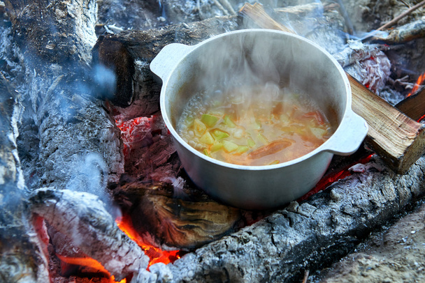 cooking on fire at picnic, food prepared in kettle on wood, potatoes and tomatoes, healthy vegetarian food - Photo, Image