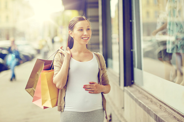 happy pregnant woman with shopping bags at city - 写真・画像