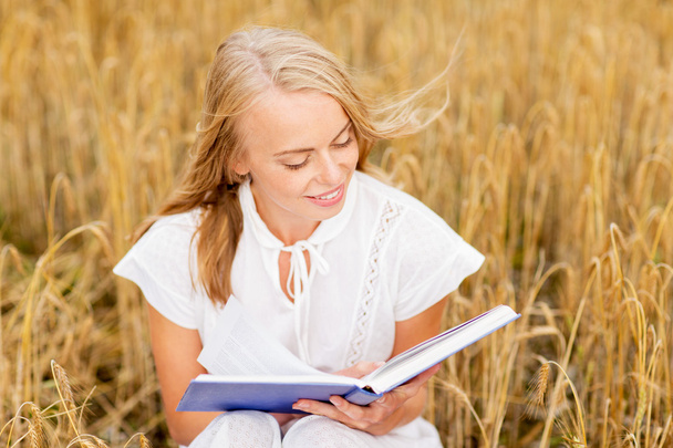 sonriente joven leyendo libro sobre el campo de cereales
 - Foto, Imagen