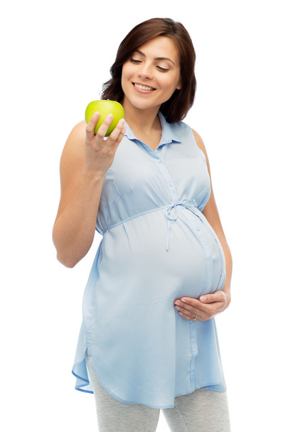 happy pregnant woman looking at green apple - Foto, Imagen