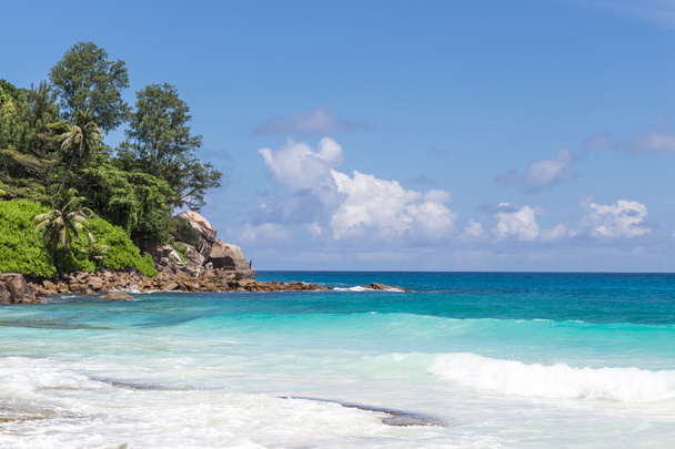 bonito azul-turquesa, ondas azuis na praia contra o pano de fundo de rocha e céu com nuvens
 - Foto, Imagem