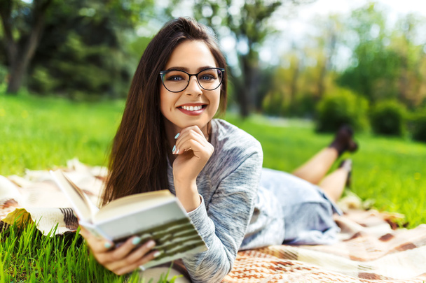 Beautiful relaxed young woman reading a book at the lawn with sun shining.  - Foto, Imagen