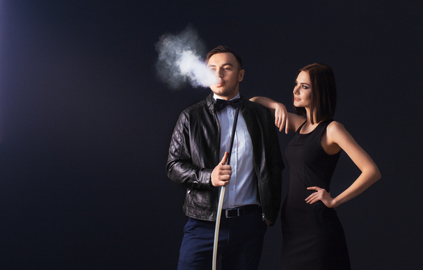 Beautiful couple smoking hookah. Producing the smoke from his mouth. Business style clothing. The pleasure of smoking. Love. - Фото, изображение
