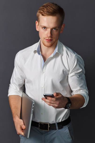 Portrait of a Young red-haired Man with a laptop and phone in hands. American appearance. Muscular body.  - Foto, afbeelding