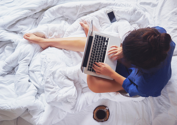 Młoda kobieta picia kawy w domu w jej łóżku i sprawdzenie jej  - Zdjęcie, obraz