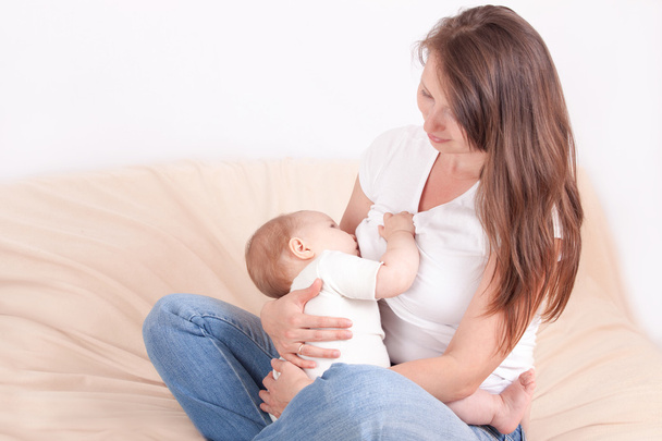 Μια νεαρή γυναίκα τροφές του μωρού στο στήθος, κάθεται στο κρεβάτι - Φωτογραφία, εικόνα