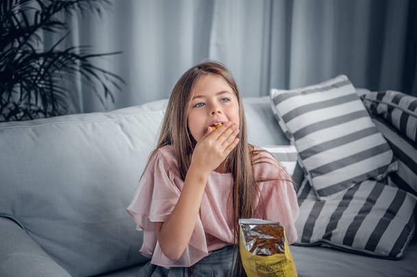 A girl eating candies sitting on a sofa - Foto, afbeelding