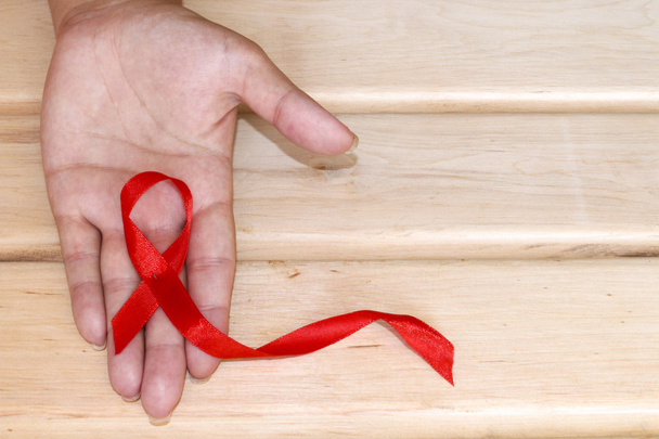 The symbolic conception of the world day of fight against AIDS. The red ribbon in the hands of a young woman on wooden background. - Photo, Image