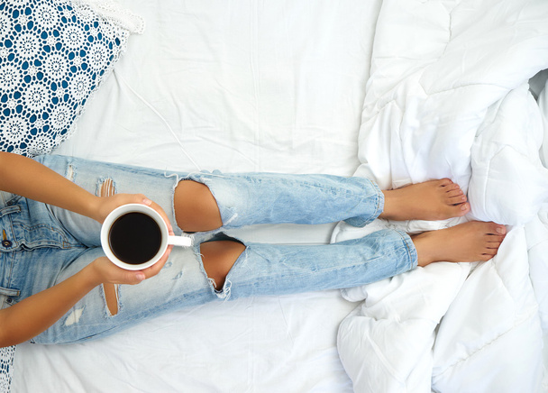 Jonge vrouw genieten van haar koffie zittend in bed. - Foto, afbeelding