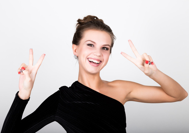 close-up fashion photo young lady in elegant black dress, playful woman smiling and shows a sign of peace - Valokuva, kuva