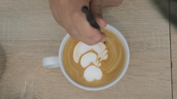 On the table is a cup of coffee with foam and the man draws on the foam pattern - Záběry, video