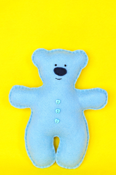 Niebieski niedźwiedź filcowy na żółtym tle, ręcznie szyta zabawka, rzemiosło z filcu. Ręcznie robione pluszaki, pluszowe misie. DIY pluszowy miś rzemiosło łatwy projekt szycia - Zdjęcie, obraz