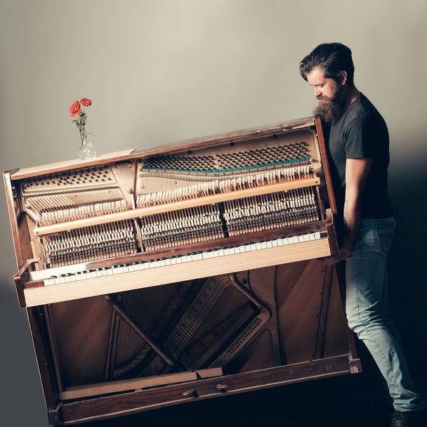 bearded man trying to move wooden piano with rose - Foto, afbeelding