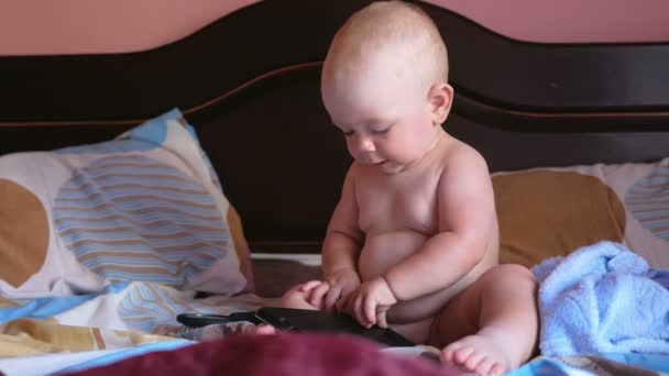 Beautiful baby playing with a tablet in bed. Smiles and tries to open the cover. Kid 1 year. - Кадри, відео