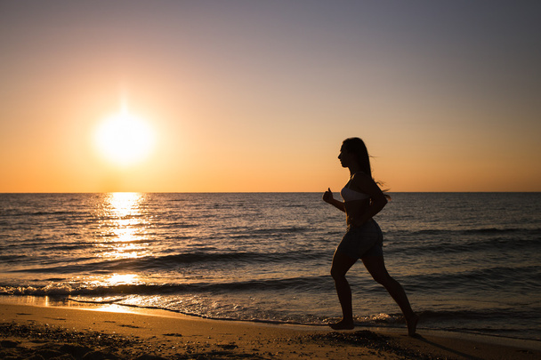 Woman running on the beach at sunset - Foto, afbeelding