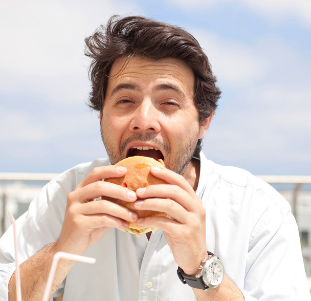 Junger Mann isst einen Hamburger - Foto, Bild