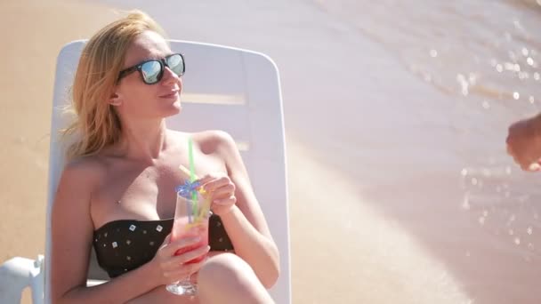 woman drinking a cocktail on the beach. woman sunbathing by the sea - Felvétel, videó