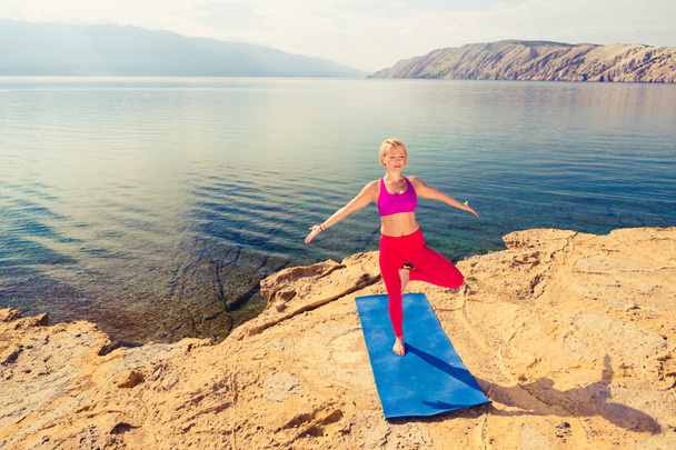 Женщина медитирует на дереве йоги поза у моря и гор
 - Фото, изображение