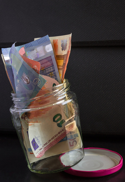 Банкноти євро є в прозору скляну банку, на чорному тлі. - Фото, зображення