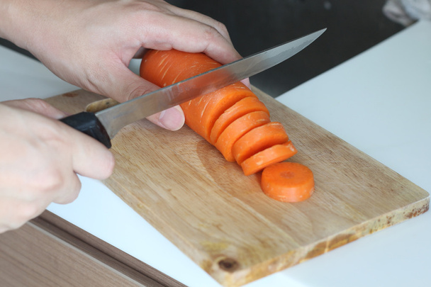 Σεφ χέρι χρησιμοποιείται για το μαχαίρι κοπής καρότο σε ένα ξύλινο ταμπλό με - Φωτογραφία, εικόνα