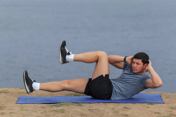 Sit-ups - fitness man uitoefening van sit omhoog buiten in gras in de zomer. passen mannelijke atleet grensoverschrijdende opleiding in de zomer uit te werken. Kaukasische gespierde Sport model in zijn 20s - Foto, afbeelding