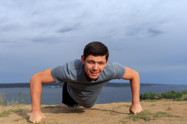 Smiling young man doing push-ups outdoors. - Photo, Image