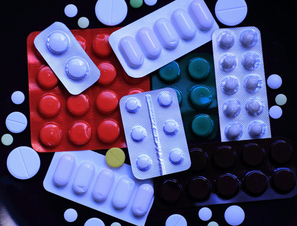 versiegelte Tablettenverpackungen und verstreute Pillen auf schwarzer Oberfläche isoliert - Foto, Bild
