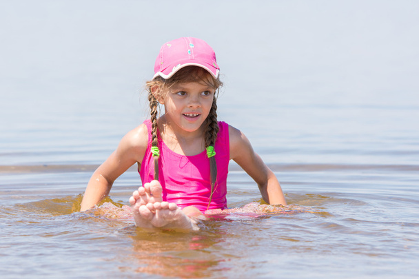 Girl in a cap sits on a shallow river in water - Foto, Imagen