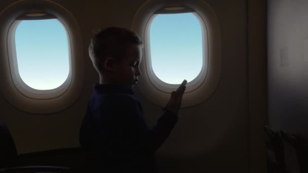 A repülőgép utasterében kisfiú tartja a telefont, és néz egy video - Felvétel, videó