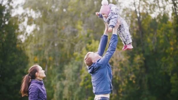 Mutlu bir aile: Baba, anne ve çocuk - küçük kız sonbahar parkta yürüyüş: baba atar Bebek kucağında, ağır çekim - Video, Çekim
