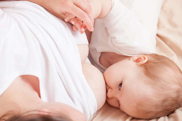 Το μωρό τρώει μαμά γάλα μαστού ξαπλωμένος στο κρεβάτι - Φωτογραφία, εικόνα