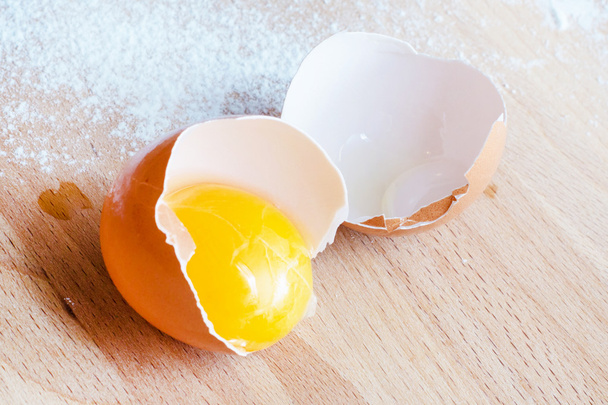 Close up egg, yolk in eggshell, flour on a wooden background - Photo, Image