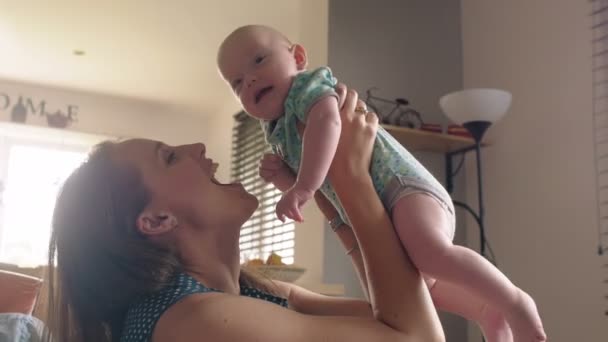 mother is holding up her adorable smiling baby sitting on the sofa . 4k - Footage, Video