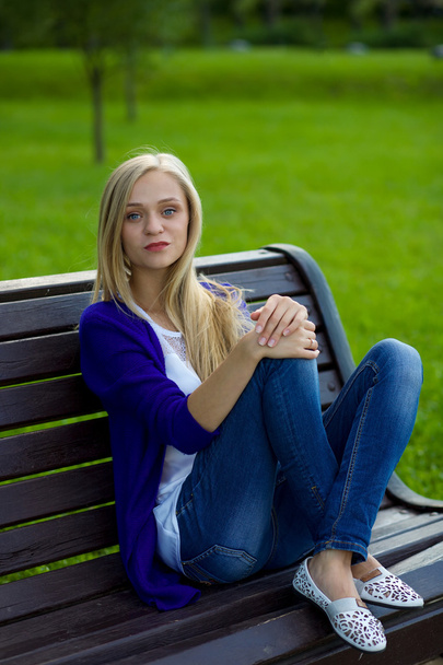 Portrait of a beautiful blonde girl in the park. She is sitting  - Foto, Imagen