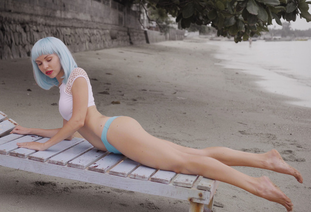 Seksikäs kaunis nainen moderni futuristinen tyyli poseeraa vaurioitunut puinen sininen solarium. Luova ulkoasu nainen rannalla yllään bikinit ja sininen peruukki
 - Valokuva, kuva
