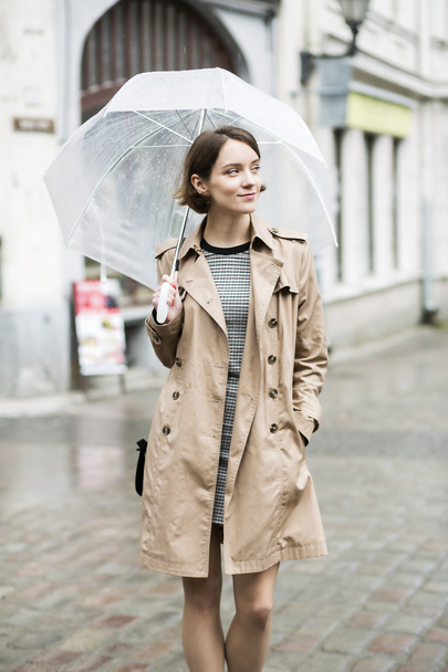 Женщина в бежевом пальто гуляет по мокрой улице
 - Фото, изображение
