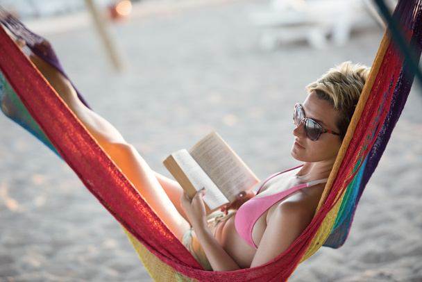 relaxed woman laying in hammock bed on beach and enjoy sunset while reading book - Fotografie, Obrázek
