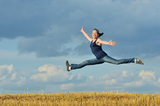 Beautiful girl in gymnastic jump against blue sky - Photo, Image