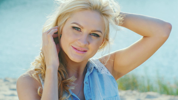 Приваблива блондинка посміхається в камеру, крупним планом. Літній день на пляжі біля моря
 - Кадри, відео