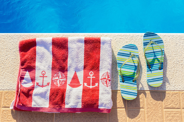 Chinelos de banho e toalha de banho na piscina
 - Foto, Imagem