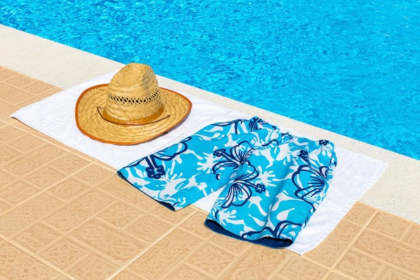 Hat and swimming trunks on towel near swimming pool - Foto, afbeelding