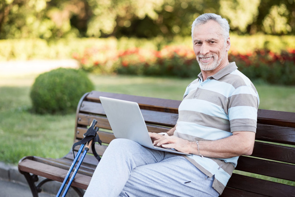 Stylish handsome old man sitting in a park wearing sportswear. - Foto, imagen