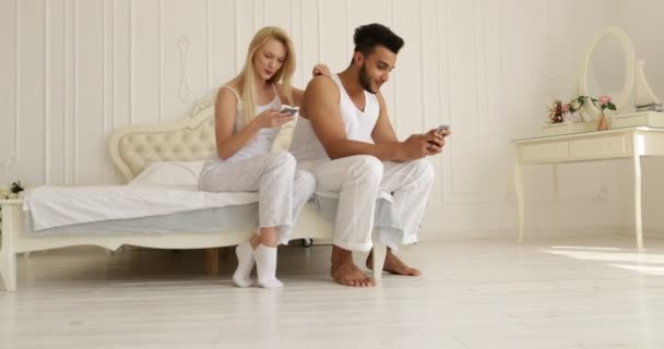 Couple using smart phone sitting bed mix race man woman embrace smile morning bedroom - Metraje, vídeo