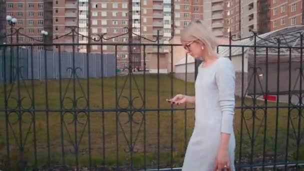Side view of a young woman walking in the city using smartphone texting and using app - Materiał filmowy, wideo