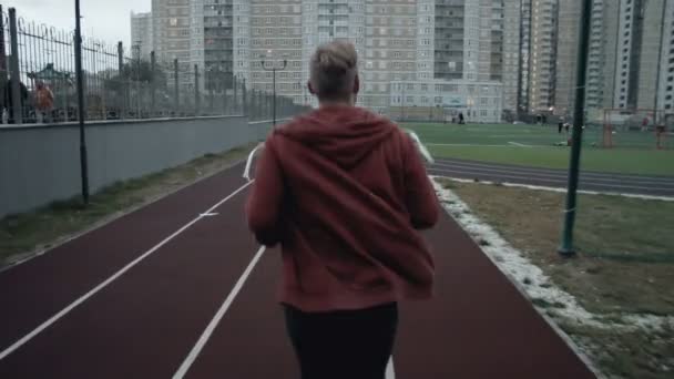 Young man running on the track following shot - Video
