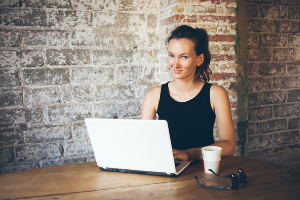 ポニーテールの髪型と美しい若い女性は、ラップトップでコーヒー ショップで働いています。女性フリーランスのコンピューター経由でインターネットに接続します。 - 写真・画像