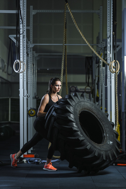 Ισχυρό μυώδης γυναίκα εκπαιδευτής Διασταυρέσω κάνει προπόνηση ελαστικών στο γυμναστήριο - Φωτογραφία, εικόνα