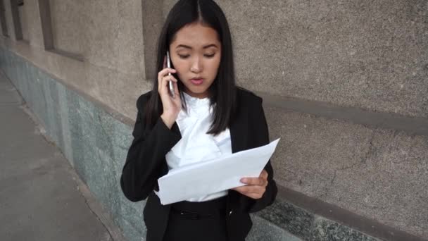 Fiatal gyönyörű üzleti nő női lány portré beszélni a telefonhívás tartani dokumentumokat háttér irodaház szabadtéri - Felvétel, videó