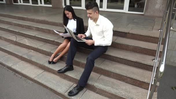 Kadın ve beyaz erkek kullanım belgeleri, dizüstü basın klavye ofis binası merdivenlerde otur genç Asyalı güzel iş kadını - Video, Çekim