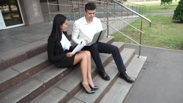 Jonge mooie zakenvrouw vrouwelijke en Kaukasische mannelijke gebruik documenten, Laptop pers toetsenbord op de trappen van het kantoorgebouw zitten - Video